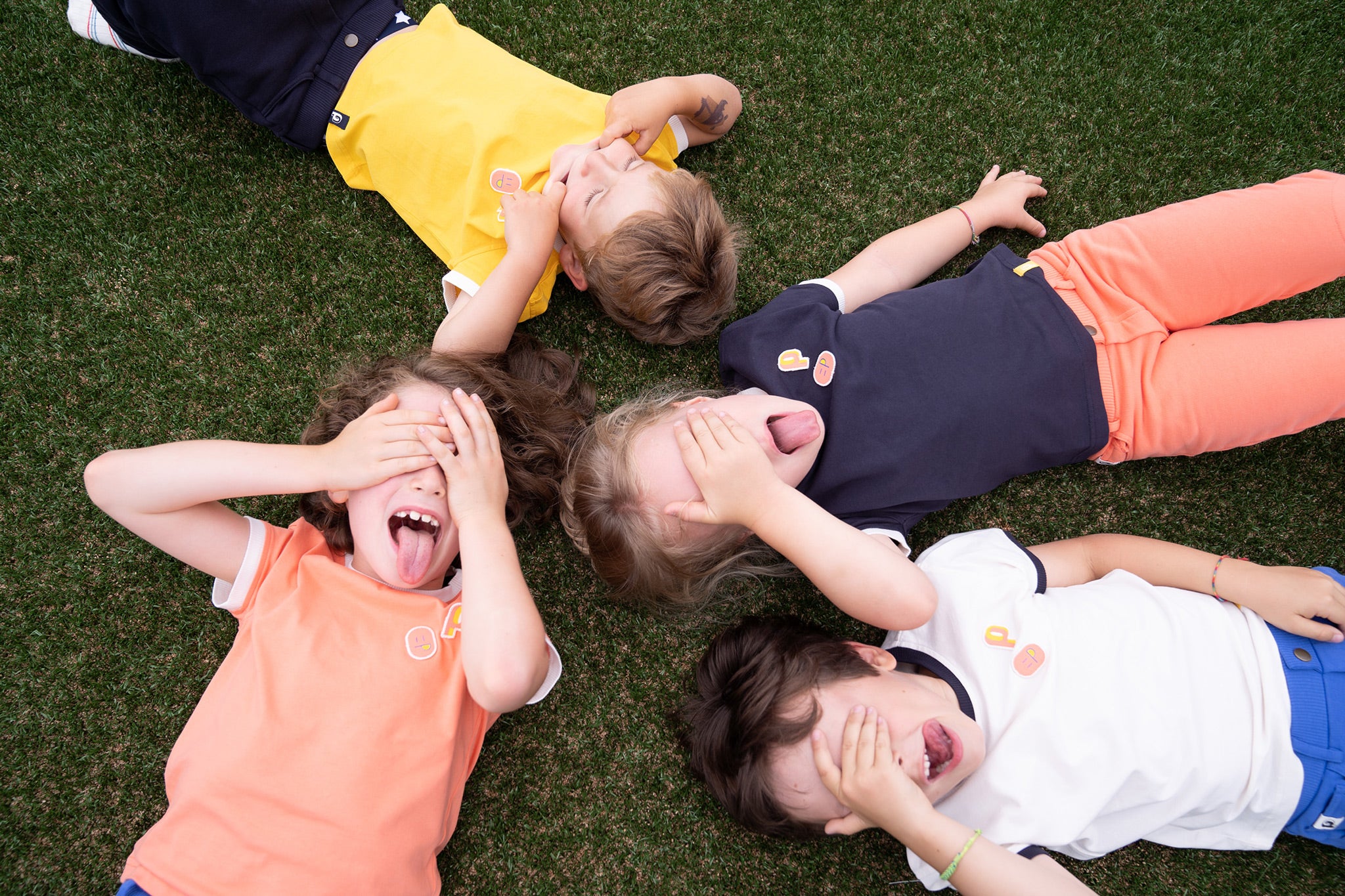 tee-shirt More Perpète enfant, en coton bio, porté par quatre enfants allongés au sol, dans les coloris jaune, crème, corail et marine