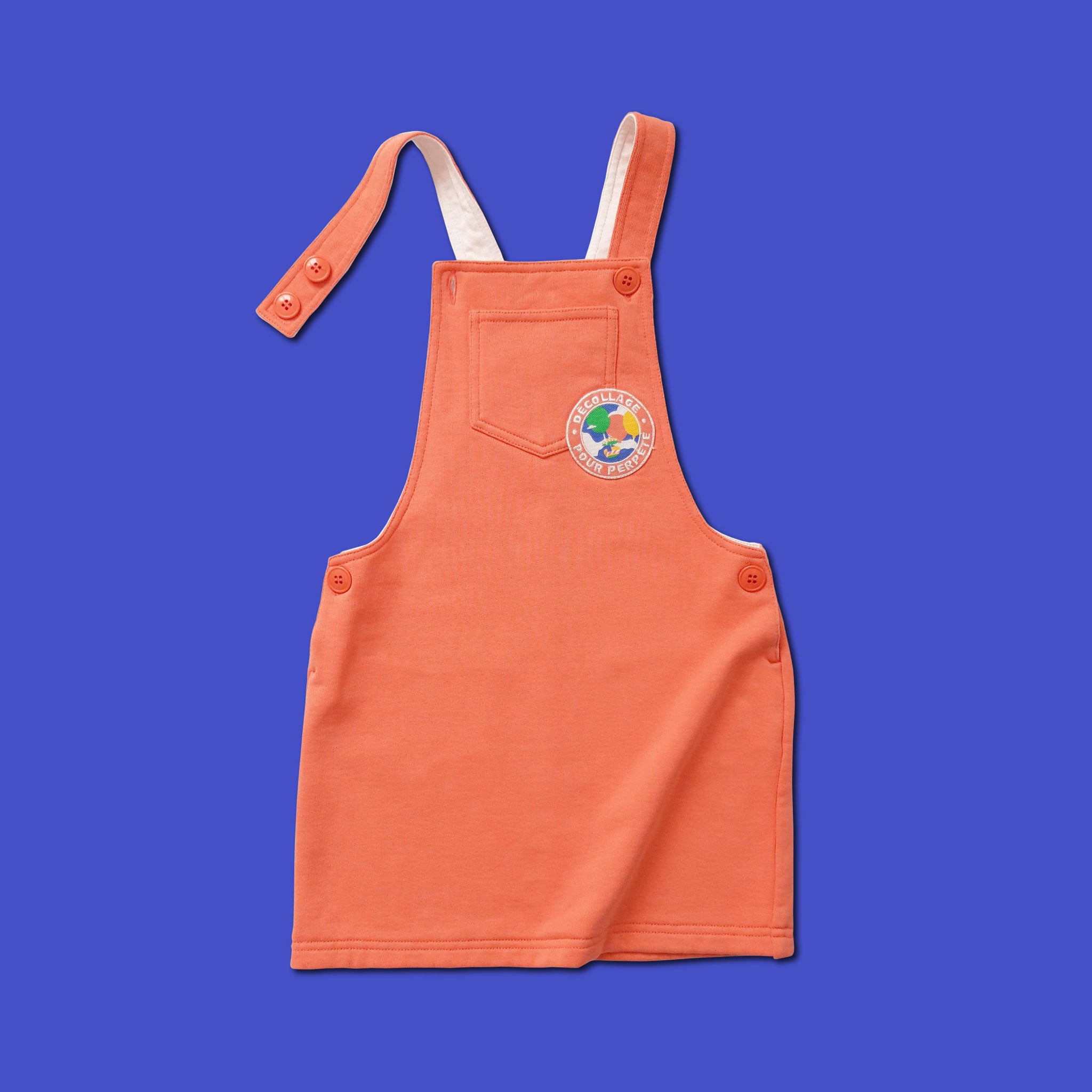 Robe Perpète Power enfant, en coton bio, coloris corail avec patch imprimé sur la poitrine, à plat, avec  bretelles reglables par boutons, vue de face