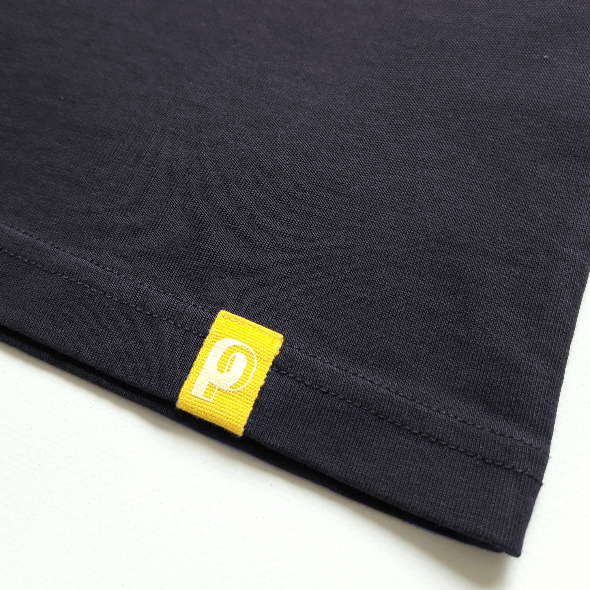 Zoom sur l'étiquette jaune, en bas du tee-shirt More Perpète enfant marine,  avec le P de Perpète imprimé